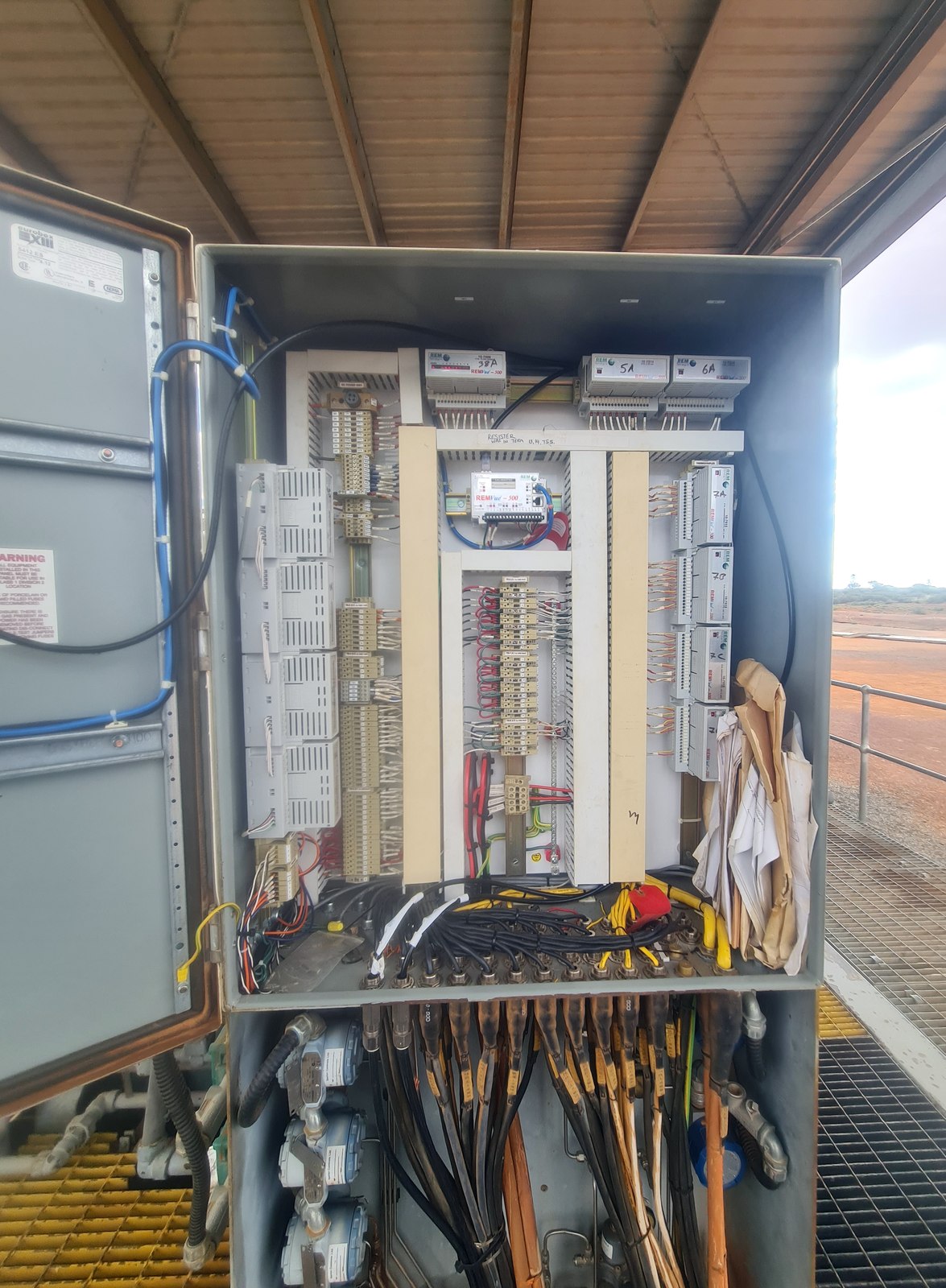 The obsolete compressor control panel open on site, red dirt and shed behind it
